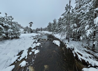 An aerial view of a frozen river flowing through snow-covered forests on a cloudy sunset sky background.