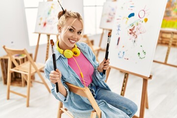 Young caucasian woman artist smiling confident holding paintbrushes at art studio