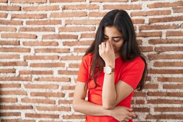 Young teenager girl standing over bricks wall tired rubbing nose and eyes feeling fatigue and headache. stress and frustration concept.