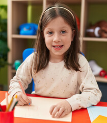 Adorable hispanic girl preschool student sitting on table drawing on paper at kindergarten