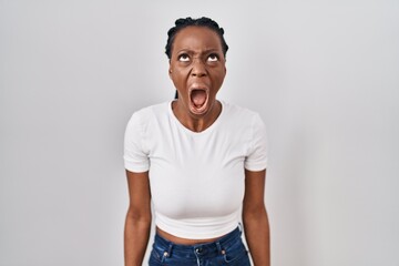 Beautiful black woman standing over isolated background angry and mad screaming frustrated and furious, shouting with anger. rage and aggressive concept.