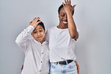 Fototapeta premium Young mother and son standing together over white background surprised with hand on head for mistake, remember error. forgot, bad memory concept.