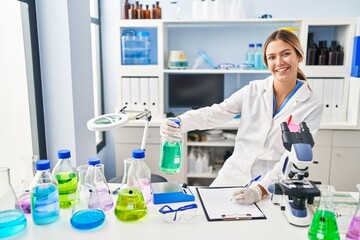 Fototapeta premium Young hispanic woman scientist measuring liquid write on document at laboratory