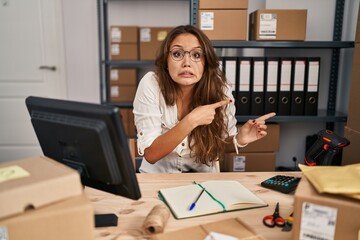 Young hispanic woman working at small business ecommerce pointing aside worried and nervous with...