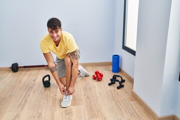 Young hispanic man smiling confident tying shoe at sport center