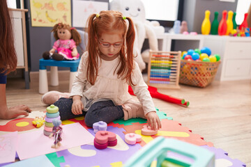 Adorable redhead girl playing with toys sitting on floor at kindergarten