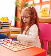 Fototapeta premium Adorable redhead girl playing with maths puzzle game sitting on table at kindergarten