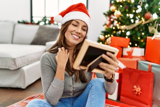 Young latin woman looking picture sitting by christmas tree at home