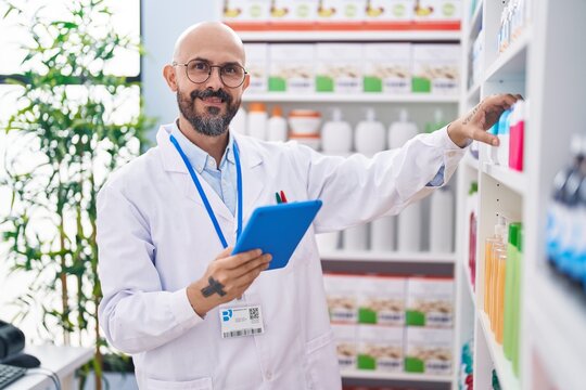 Young bald man pharmacist using touchpad holding medicine at pharmacy