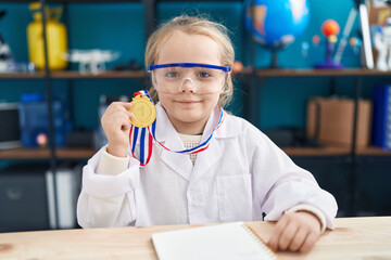 Adorable blonde girl student smiling confident holding medal at laboratory classroom