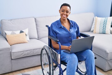 African american woman using laptop sitting on wheelchair at home