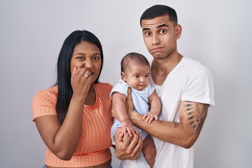 Young hispanic couple with baby standing together over isolated background looking stressed and nervous with hands on mouth biting nails. anxiety problem.