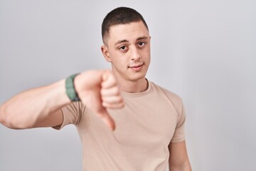 Young man standing over isolated background looking unhappy and angry showing rejection and negative with thumbs down gesture. bad expression.