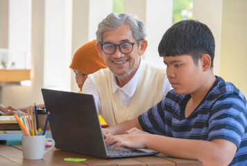 Fototapeta na wymiar mature father helping his teen sons to do school project on computer laptop, happy asian family working together at home