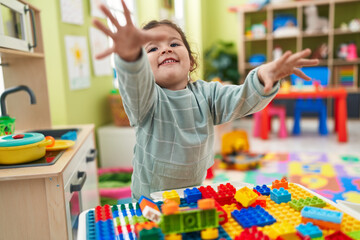 Adorable hispanic toddler playing with construction blocks standing at kindergarten