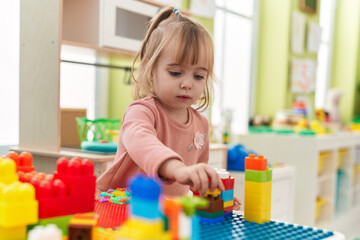 Adorable blonde girl playing with construction blocks standing at kindergarten