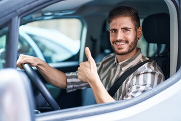 Hispanic man with beard driving car smiling happy and positive, thumb up doing excellent and approval sign