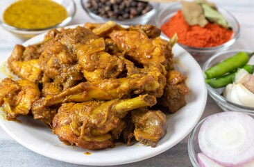Closeup of Indian Chicken Gravy or Curry in a White Plate with Green Chilies, Garlic, Ginger, Onion Slices, Black Pepper, Bay Leaf, Red Chili Powder, Dry Curry Leaves and Mustard Sauce