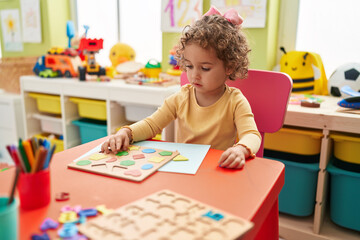 Adorable hispanic toddler playing with maths puzzle game sitting on table at kindergarten