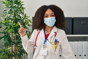 Young african american doctor woman wearing uniform and medical mask smiling happy pointing with hand and finger to the side