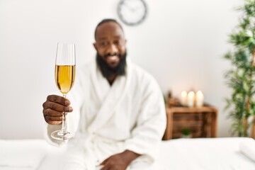Young african american man smiling confident drinking champagne at beauty center