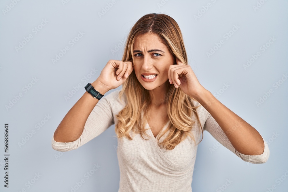 Sticker Young blonde woman standing over isolated background covering ears with fingers with annoyed expression for the noise of loud music. deaf concept.