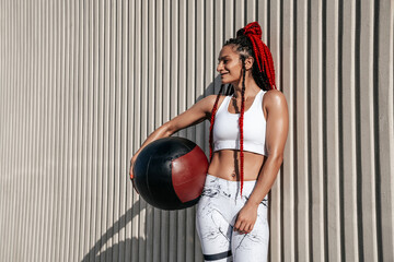 Medium shot on wall background. Athletic woman with med ball. Strength and motivation.Photo of sporty  woman in fashionable sportswear