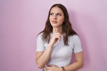Obraz premium Young hispanic girl standing over pink background thinking concentrated about doubt with finger on chin and looking up wondering