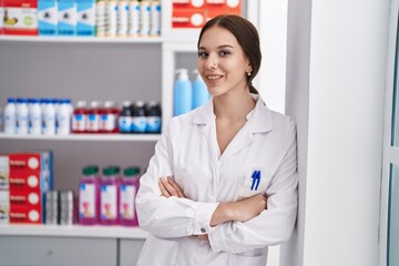 Young woman pharmacist standing with arms crossed gesture at pharmacy