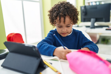 Adorable hispanic boy preschool student sitting on table drawing on notebook at classroom