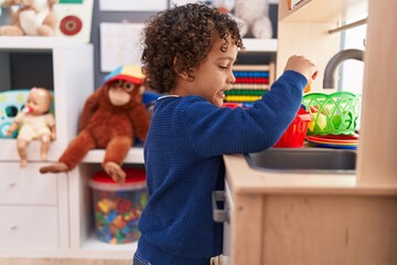 Adorable hispanic boy playing with play kitchen standing at kindergarten