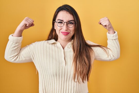 Young hispanic woman standing over yellow background showing arms muscles smiling proud. fitness concept.