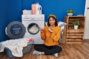 Young hispanic woman doing laundry pointing aside worried and nervous with both hands, concerned and surprised expression