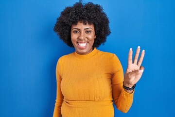 Black woman with curly hair standing over blue background showing and pointing up with fingers...