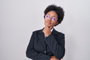 Beautiful african woman with curly hair wearing business jacket and glasses looking confident at the camera smiling with crossed arms and hand raised on chin. thinking positive.