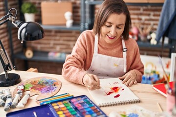 Fototapeta premium Middle age woman artist drawing on notebook at art studio
