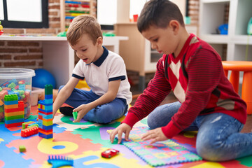 Two kids playing with construction blocks and maths puzzle game sitting on floor at kindergarten