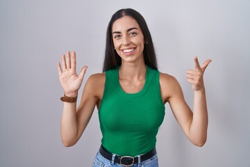 Young woman standing over isolated background showing and pointing up with fingers number seven while smiling confident and happy.