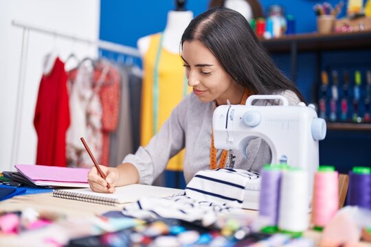 Young beautiful hispanic woman tailor smiling confident drawing on notebook at clothing factory