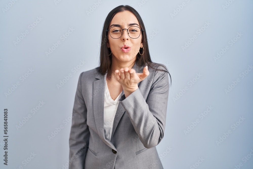 Wall mural Hispanic business woman wearing glasses looking at the camera blowing a kiss with hand on air being lovely and sexy. love expression.