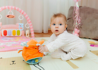 a cute little baby of 6 months is sitting on a carpet among colorful toys. a child is playing with a toy