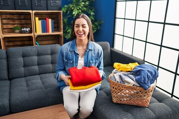 Hispanic woman holding folded laundry after ironing winking looking at the camera with sexy...