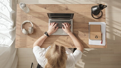 Top down view of girl working at computer, achieving success and joy. young woman throws her hands up in win or successful deal. blonde in white t-shirt rejoices while sitting at workplace.