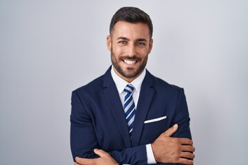 Handsome hispanic man wearing suit and tie happy face smiling with crossed arms looking at the...