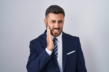 Handsome hispanic man wearing suit and tie touching mouth with hand with painful expression because of toothache or dental illness on teeth. dentist