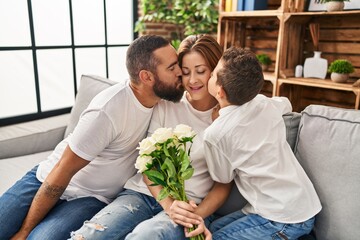 Fototapeta premium Family kissing mother holding bouquet of flowers at home