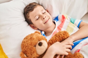 Blond child hugging teddy bear sleeping on bed at bedroom