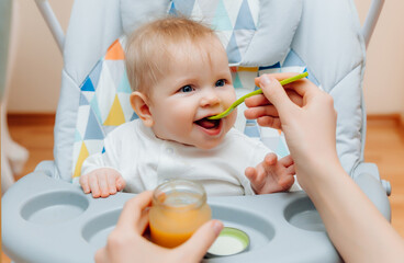 Mother gives fruit sauce to baby.mom feeds baby on highchair.baby food