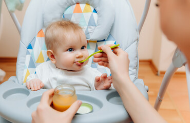 Mother gives fruit sauce to baby.mom feeds baby on highchair.baby food