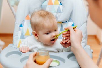 Mother gives fruit sauce to baby.mom feeds baby on highchair.baby food